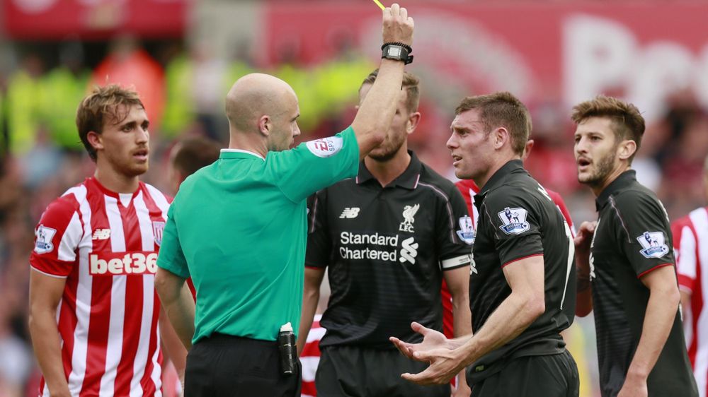 Liverpool's James Milner is shown a yellow card by referee Anthony Taylor