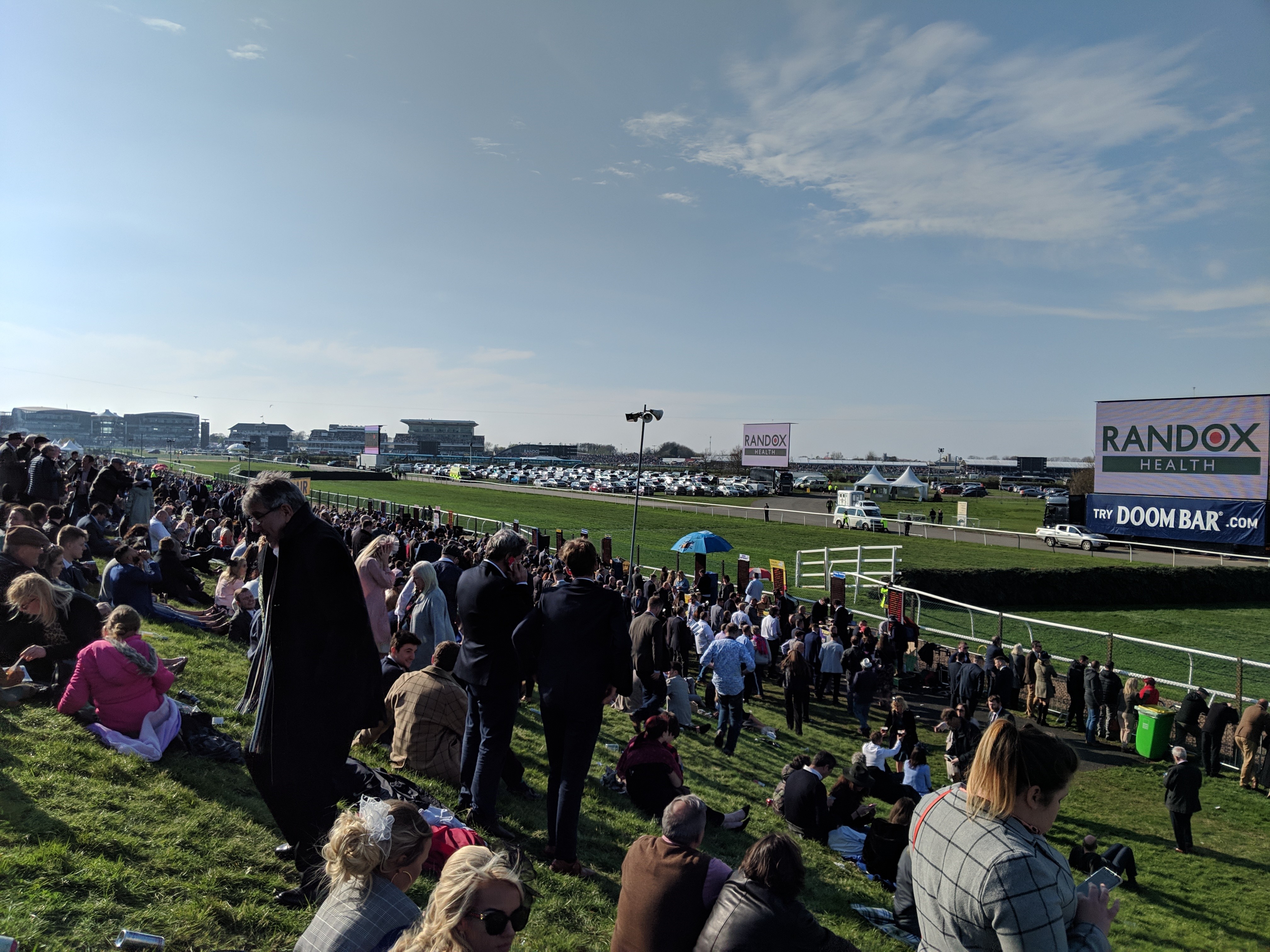 Steeple Enclosure’de çimlere serilmiş seyirciler Grand National yarışının startını bekliyor. (Bu görsel The Jockey Club'ın izniyle kullanılmıştır)