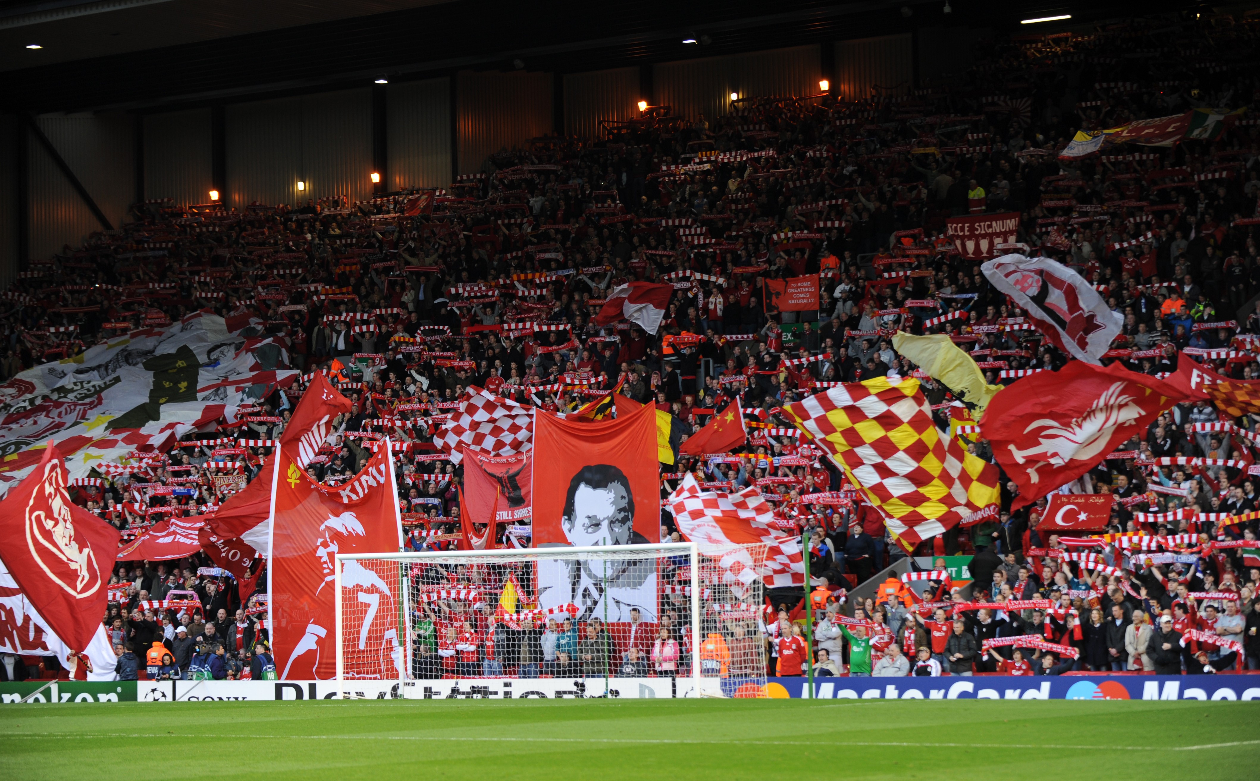 Liverpool fans hold up scarves and wave flags as they sing You'll Never Walk Alone on The Kop at Anfield Stadium